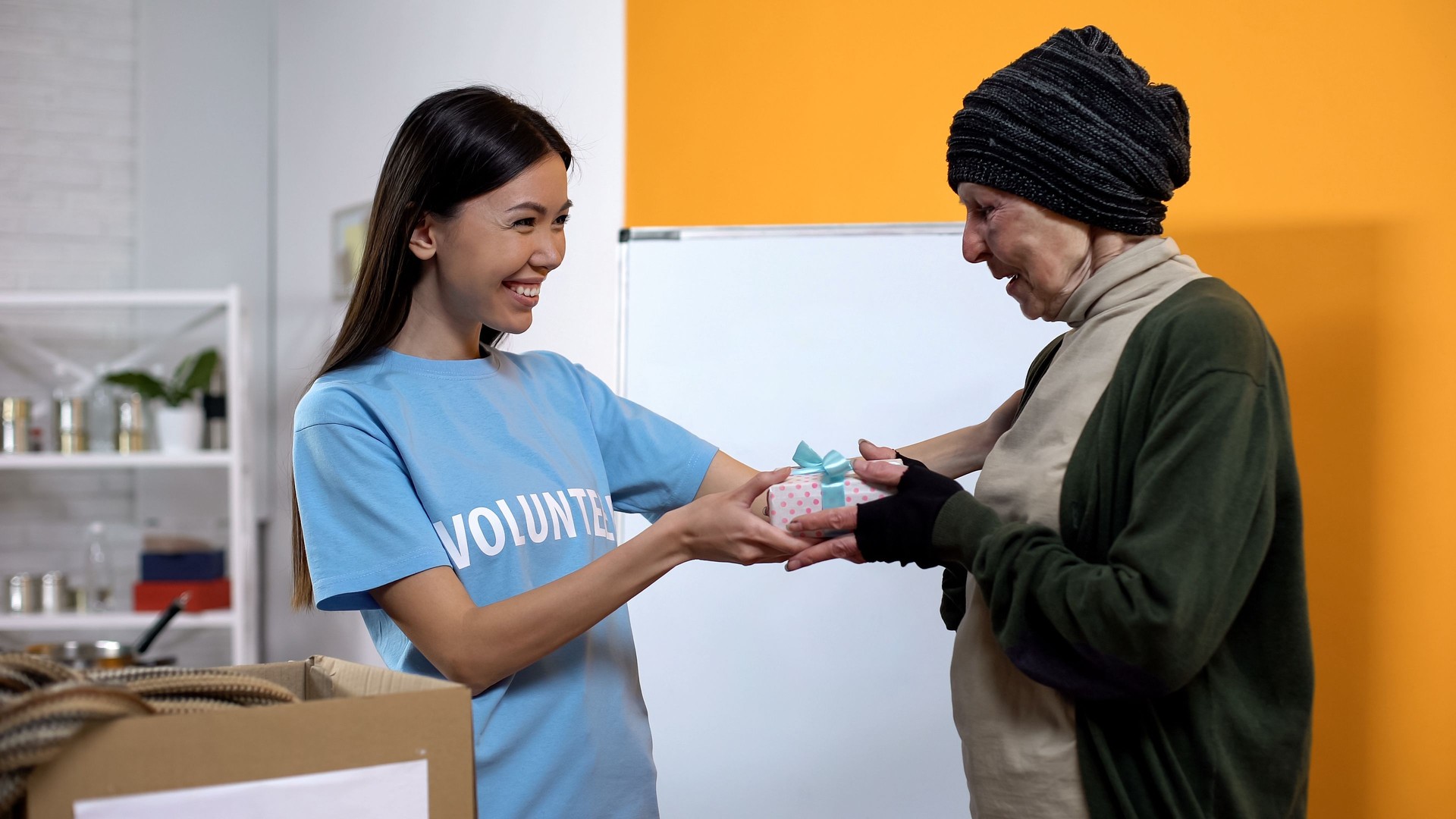 Smiling volunteer presenting gift box to needy aged female, philanthropy care