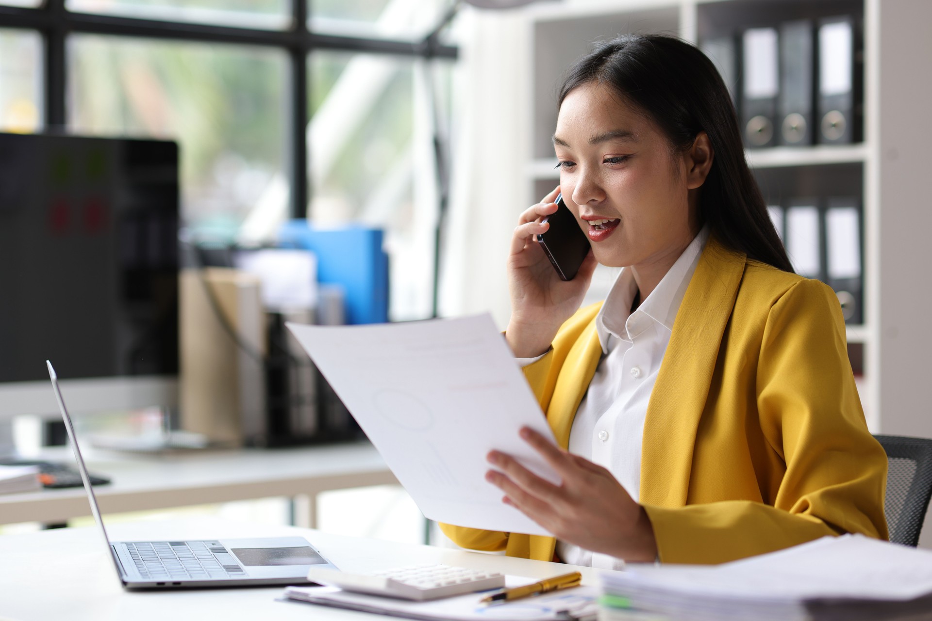 Asian businesswoman is talking on the phone with a customer and reading a monthly work schedule document.