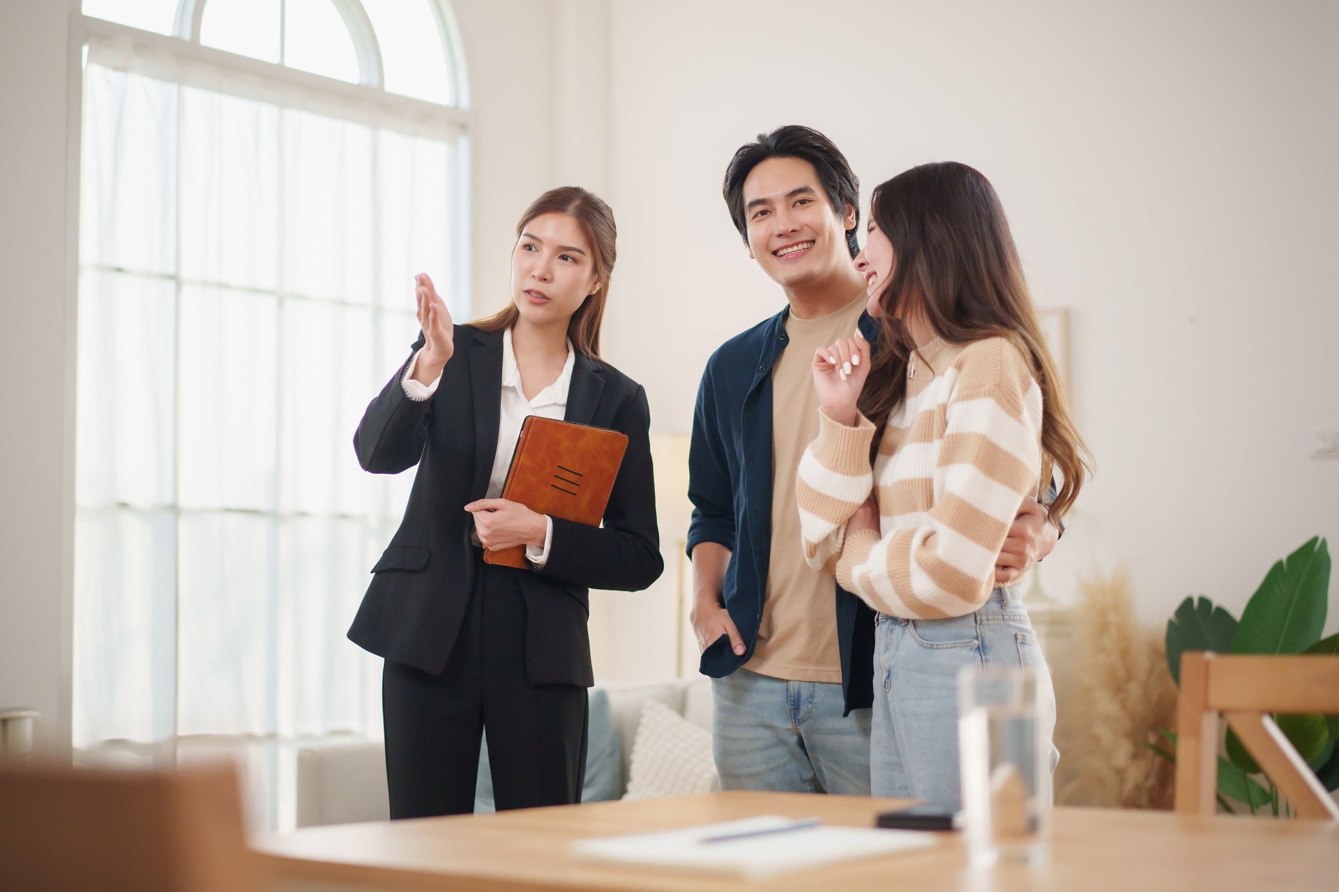 Asian couple engages in a detailed discussion with a real estate agent about home buying and financial planning while exploring a modern residence